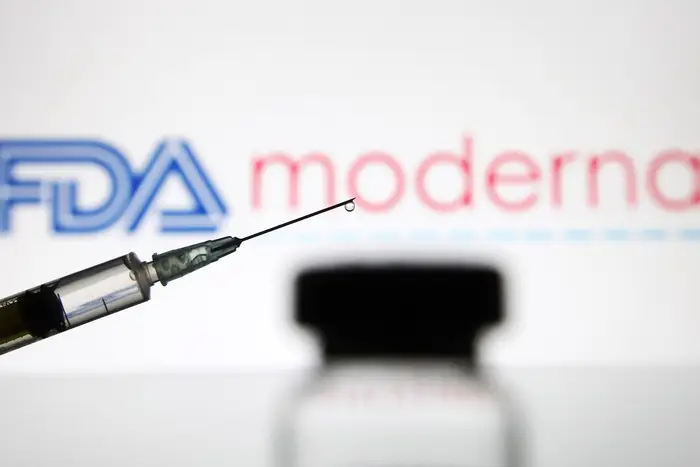 In this photo illustration, a vial and a medical syringe seen displayed in front of the Food and Drug Administration (FDA) of the United States and Moderna biotechnology company's logos.